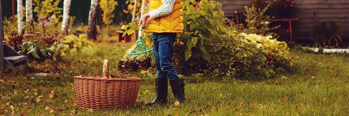 Mała dziewczynka w żółtej kamizelce grabi liście w ogrodzie
