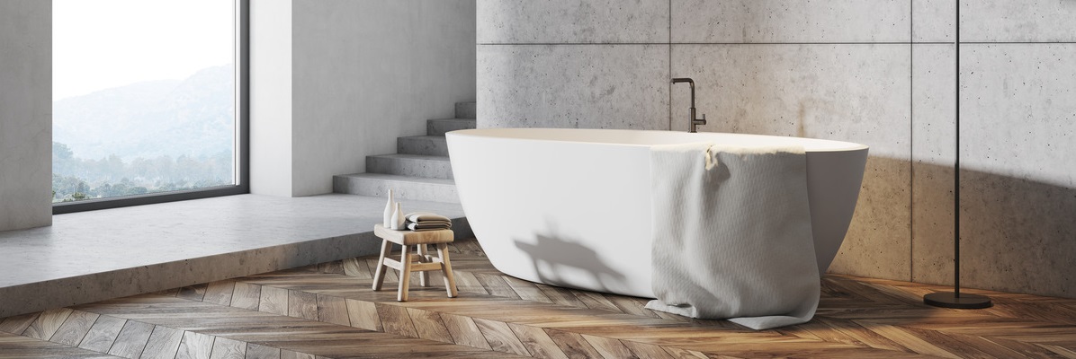 wolnostojąca wanna w łazience z drewnianą podłogą i betonowymi ścianami